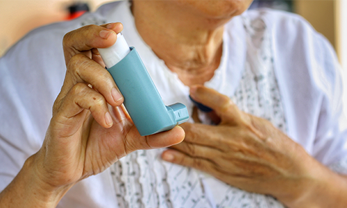 Woman's hands holding an inhaler. One of her hands is on her chest signifying her struggle to breathe.