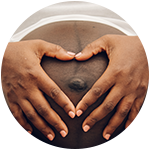A black person's hands in the shape of a heart on a pregnant belly.